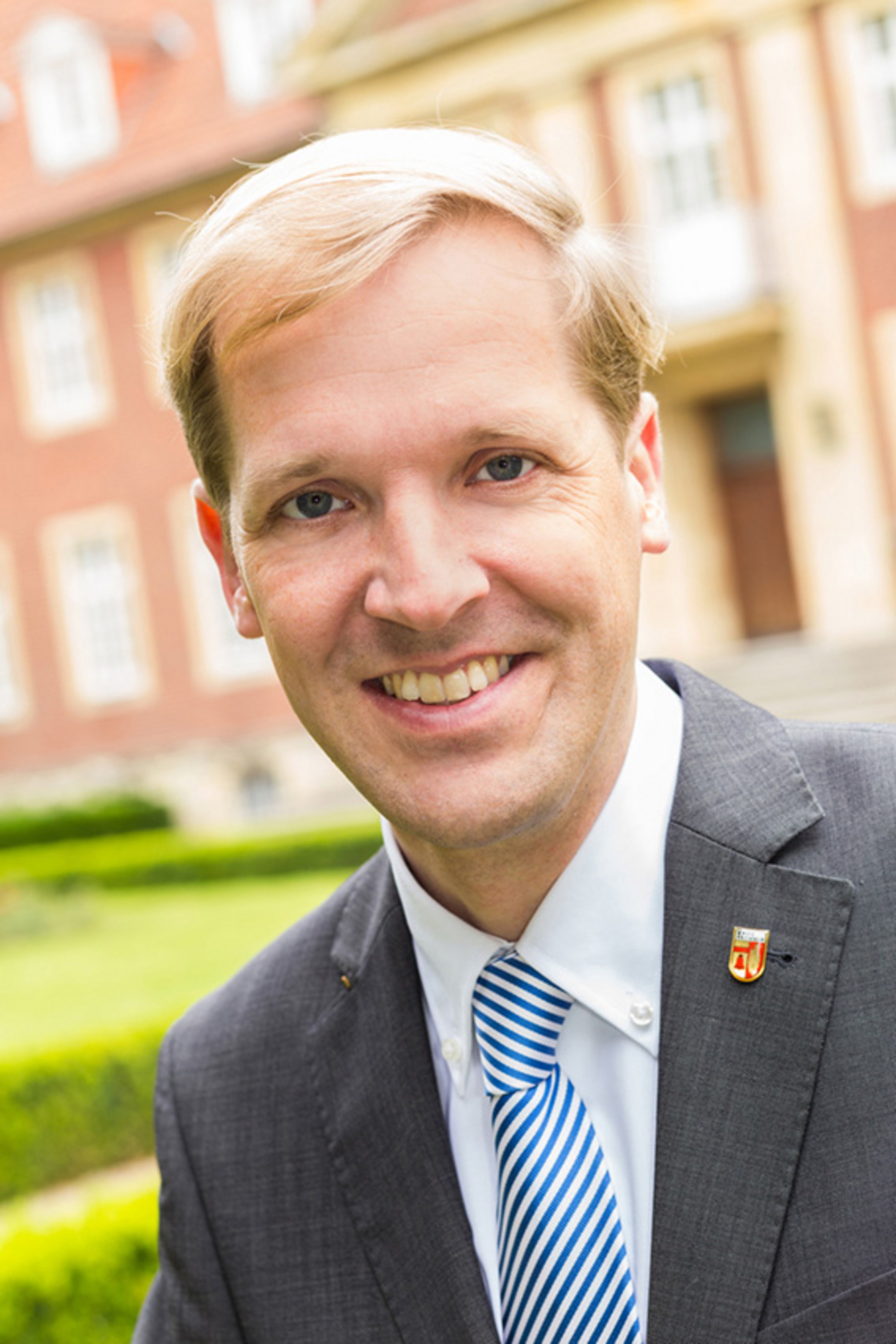 Landrat Dr. Christian Schulze Pellengahr Landrat Dr. Christian Schulze Pellengahr mit dunklem Jackett, einem weißen Hemd, blau-weißer Krawatte und einem Pin mit Kreis Coesfeld Wappen am Kragen vor dem Kreishaus II