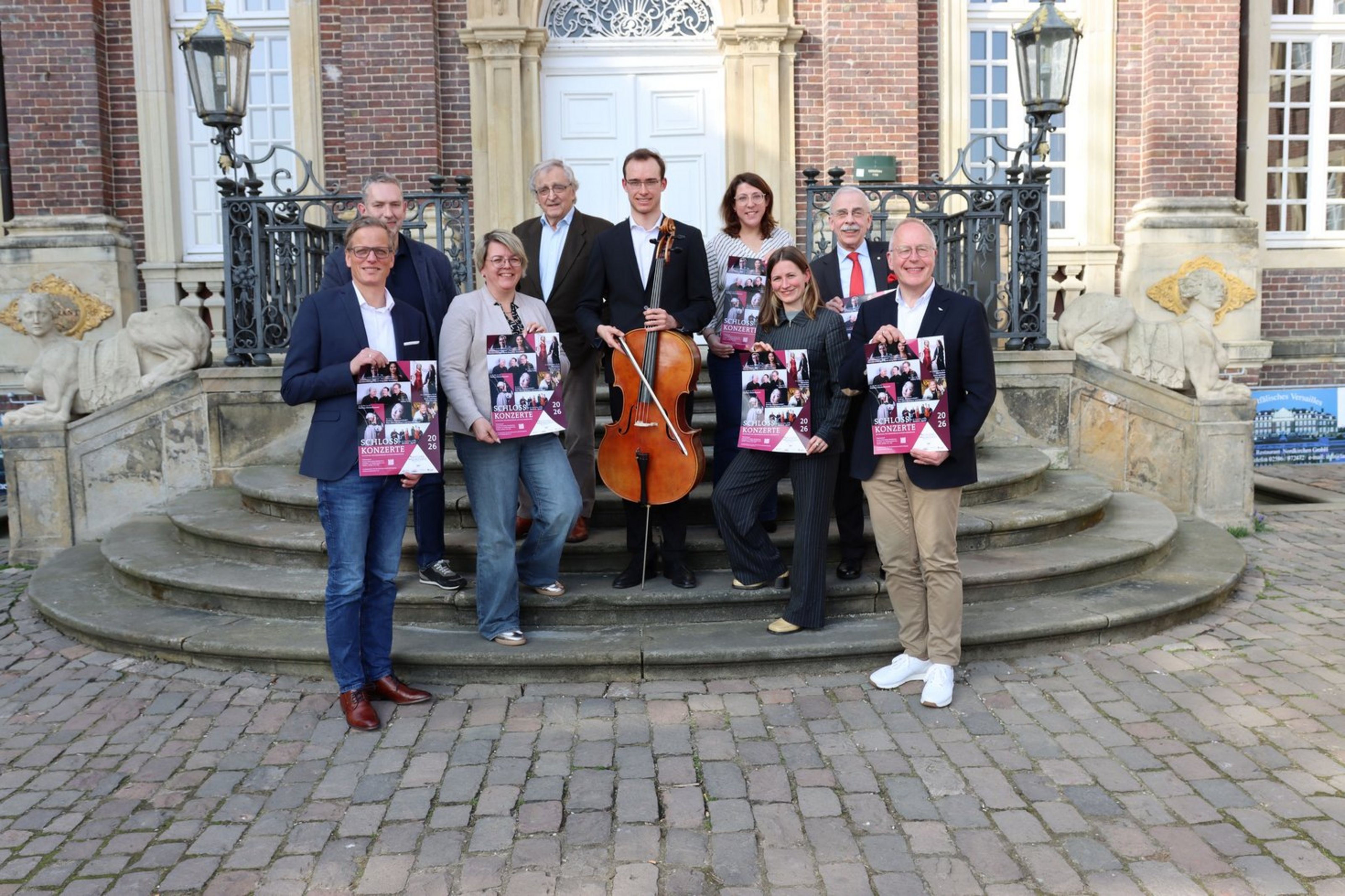 Gruppe von Personen präsentiert auf der Treppe von Schloss Nordkirchen das Programm der Schlosskonzerte.