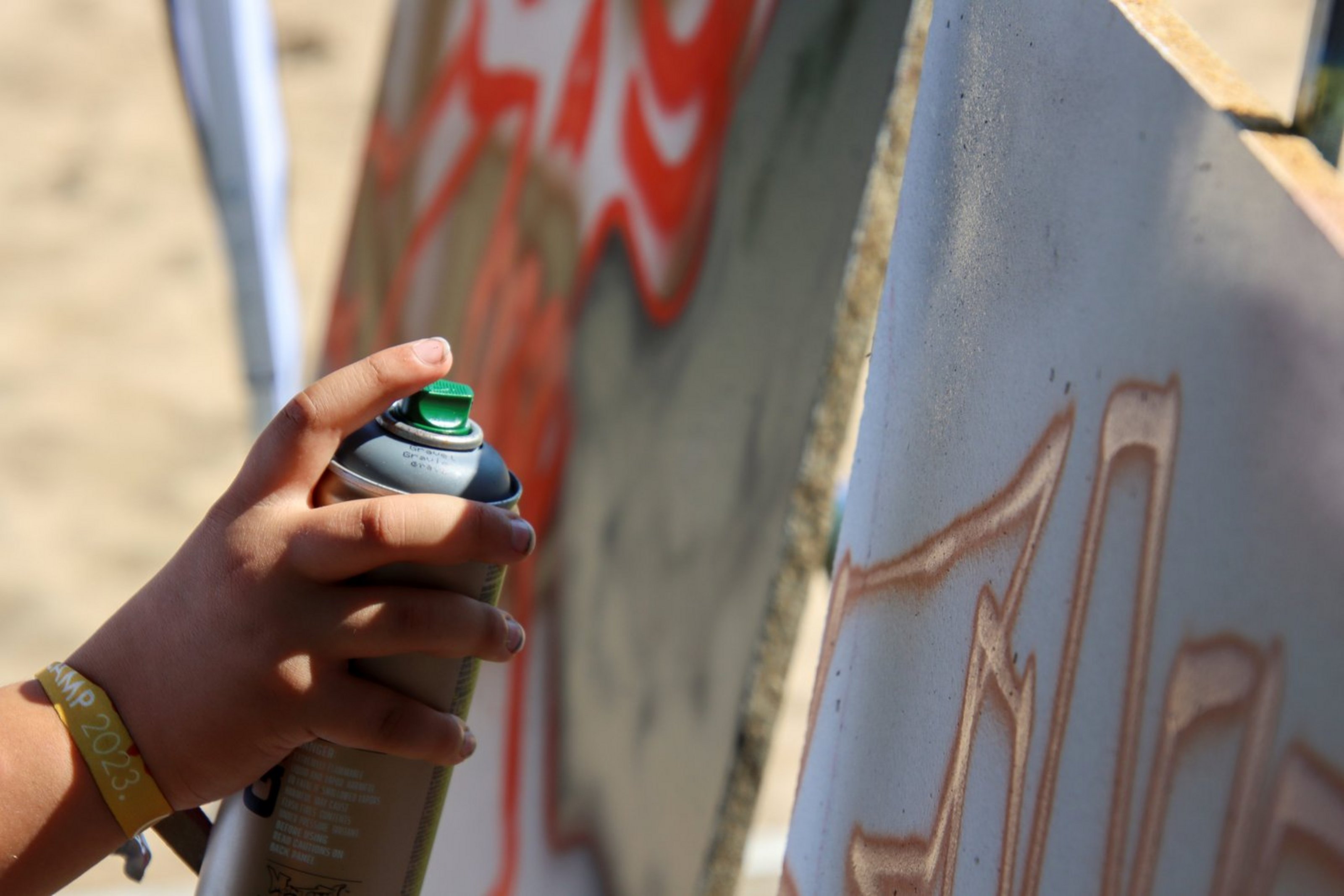 Eine Kinderhand hält eine Spraydose und sprüht Farbe auf eine Leinwand.