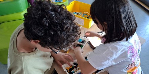 Zwei Kinder knien an einem Tisch, auf dem Klemmbausteine liegen.