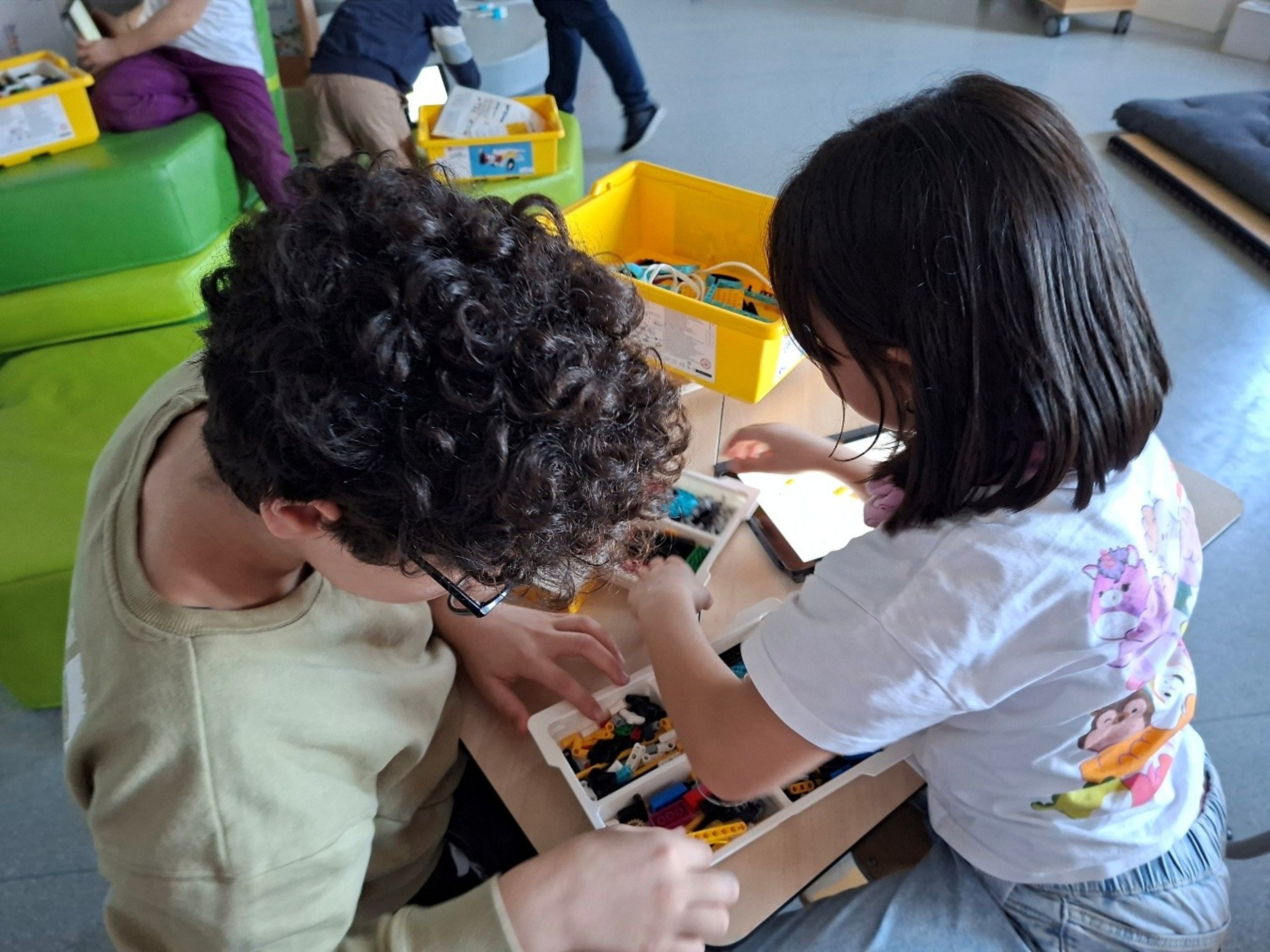 Zwei Kinder knien an einem Tisch, auf dem Klemmbausteine liegen.