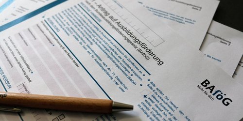 Man sieht auf einem Tisch ausgebreitete BAföG Antragsbögen auf denen ein Stift liegt.